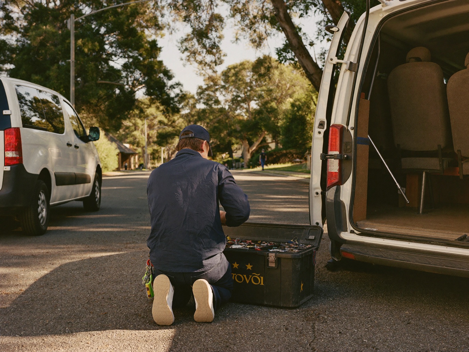 A tradesman at his toolbox beside a work van on a leafy street